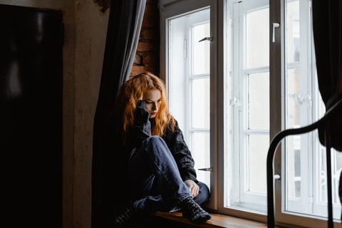woman sitting on window sill pressing her head into her hand in distress