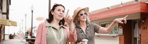 Two women walking along a boardwalk pointing at shops